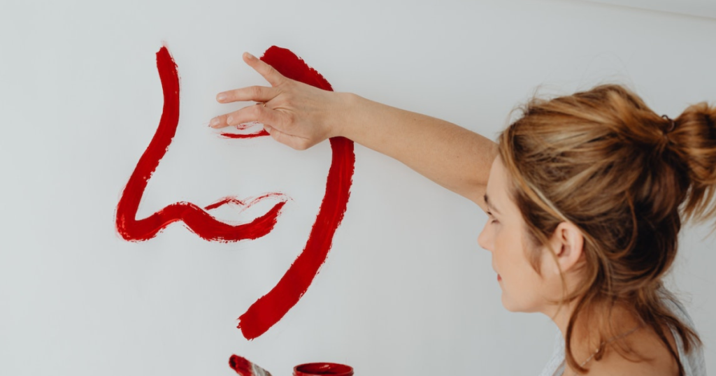 Woman Painting A Face In Red Color On A Wall