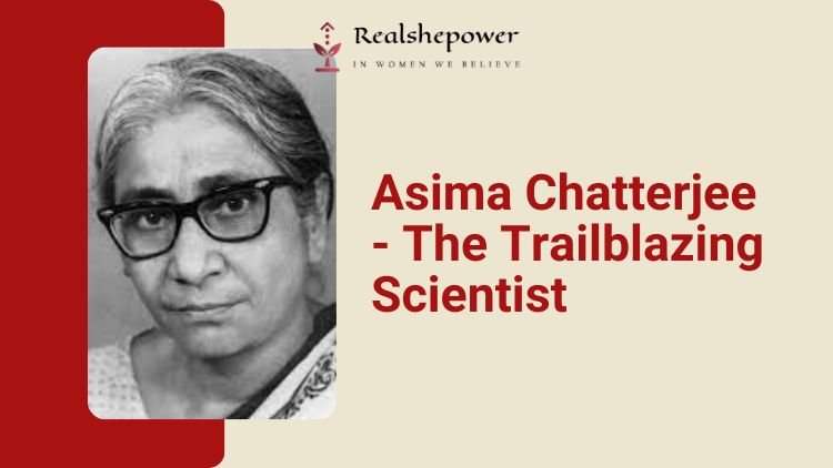 A Black And White Photograph Of Asima Chatterjee, A Trailblazing Scientist, Sitting At A Desk And Looking Towards The Camera. She Is Wearing A Saree And Glasses.