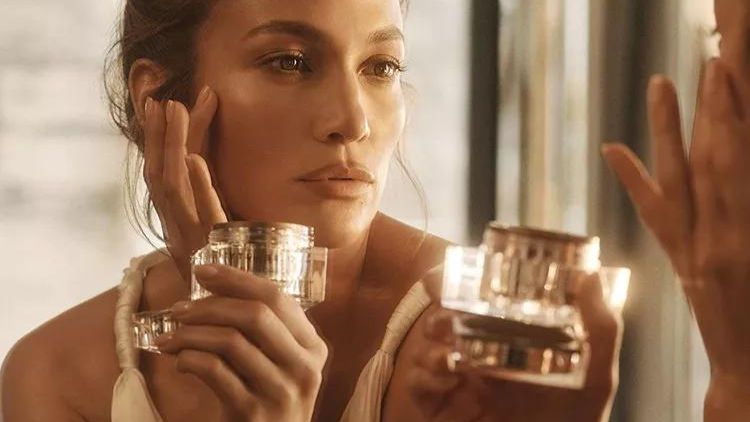 Image Of A Jlo Holding A Jlo Beauty Product. The Product Is Displayed Prominently With The Jlo Beauty Logo Visible. Jlo Has Clear And Glowing Skin, Indicating The Effectiveness Of The Product.
