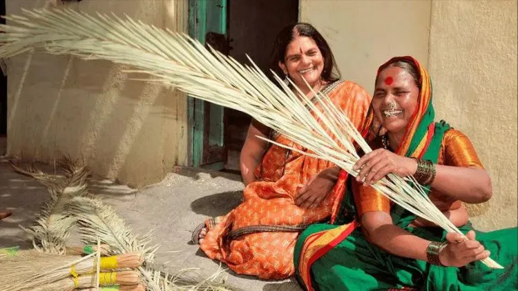 The Power Of Benevolence Blended With Valor: Chetna Gala Sinha, Founder Of First Rural Women Co-Operative Bank 4 Chetna Gala Sinha, Founder Of India'S First Rural Women'S Cooperative Bank, Sitting On The Floor Outside A House In A Village, Wearing An Orange Saree. She Is Seen Laughing Along With A Traditional Rural Woman Who Is Sitting Next To Her In A Green Saree With Orange Blouse And Making Broomsticks.